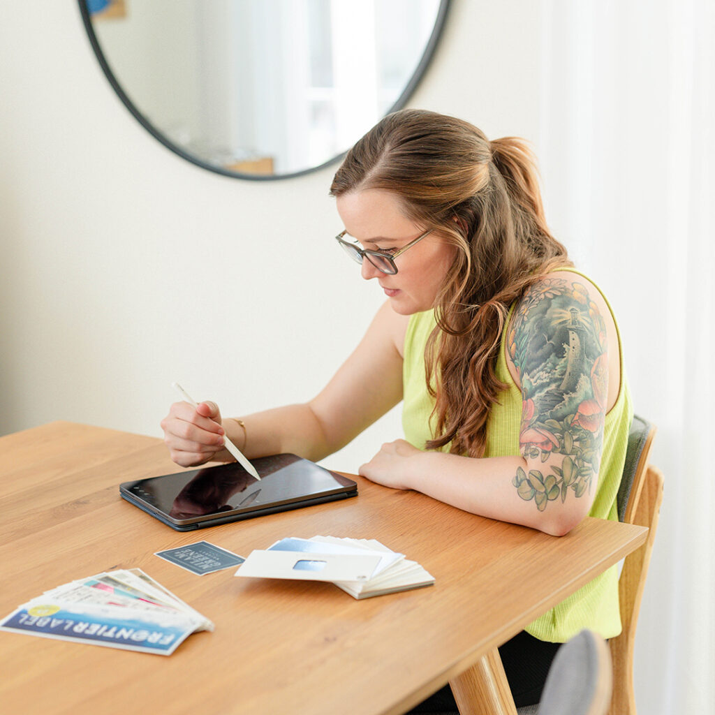 Woman with sleeve tattoo working at a table with her iPad and a printer samples in front of her.